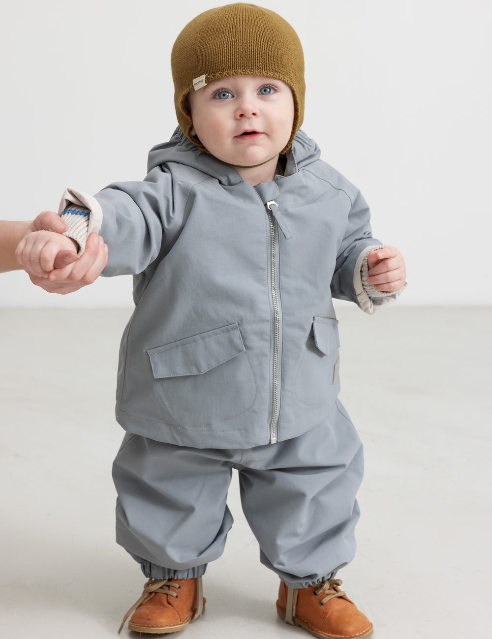 Baby wearing a brown knitted cap and dressed indoors.