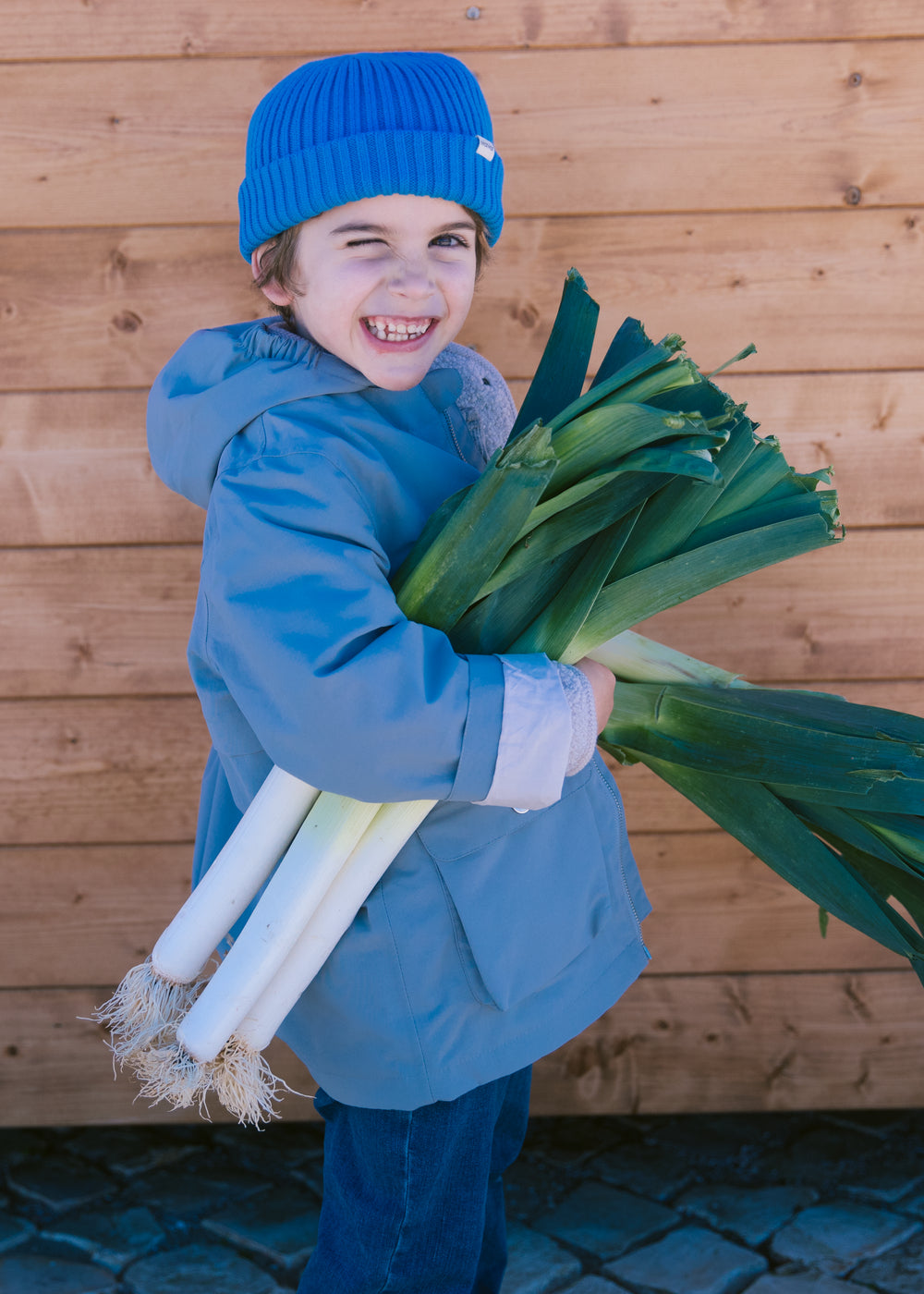 Child wearing a blue knitted hat and a blue jacket with carrots in their hands.