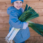 Child wearing a blue knitted hat and a blue jacket with carrots in their hands.