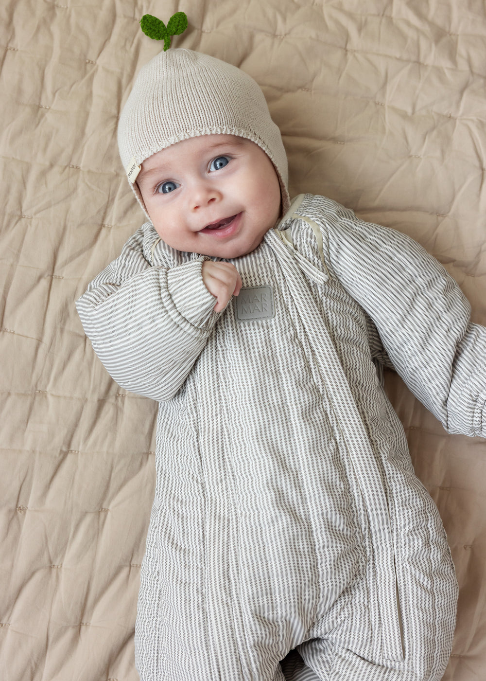 Baby wearing a striped thermal and a beige hat lying on a blanket.
