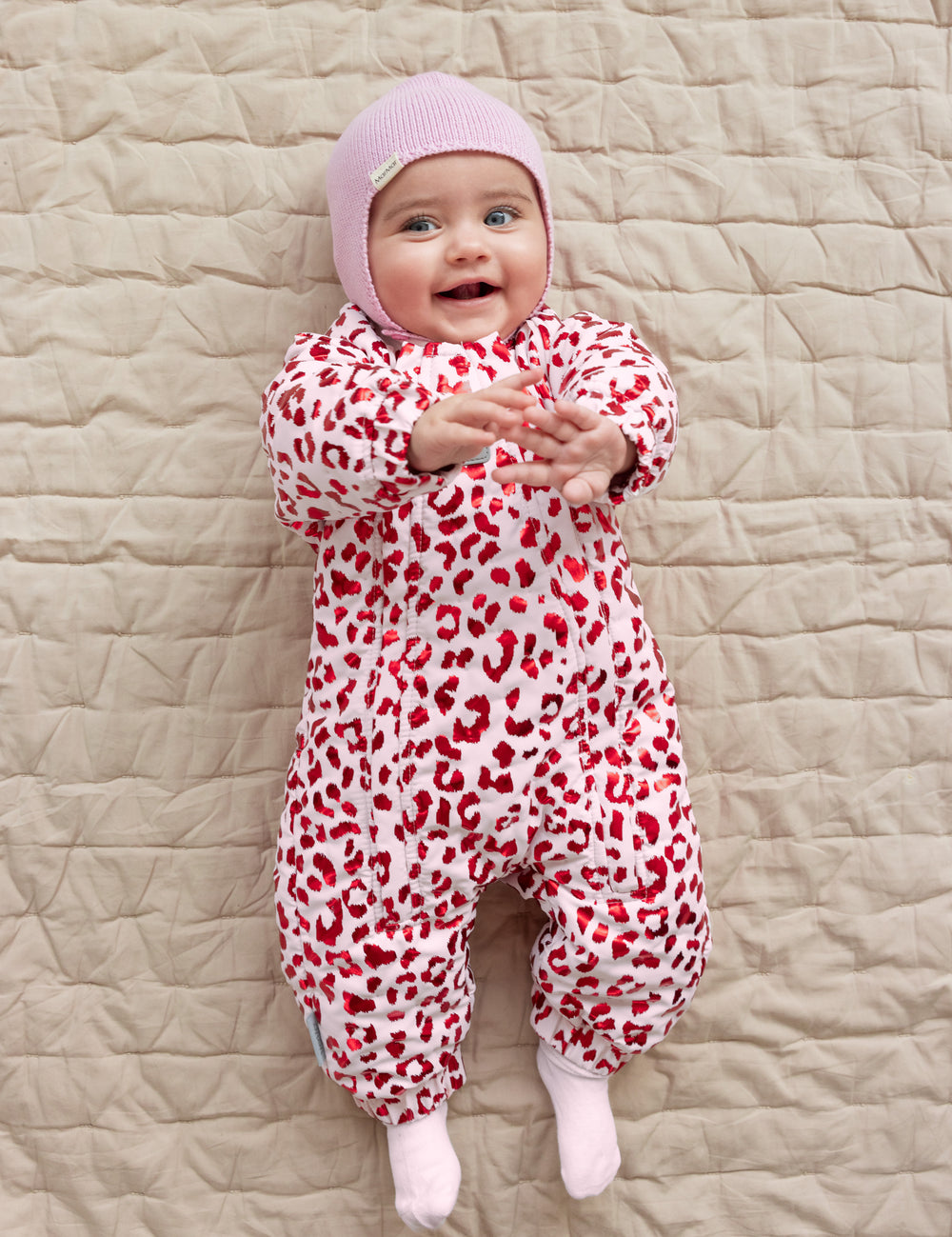 Baby wearing a leopard-patterned onesie and a bright red ribbed hat.