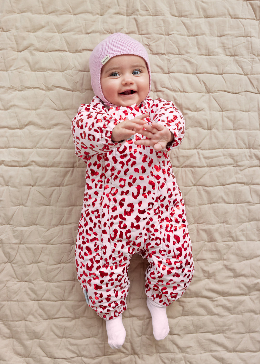 Baby wearing a leopard-patterned onesie and a bright red ribbed hat.