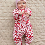 Baby wearing a leopard-patterned onesie and a bright red ribbed hat.