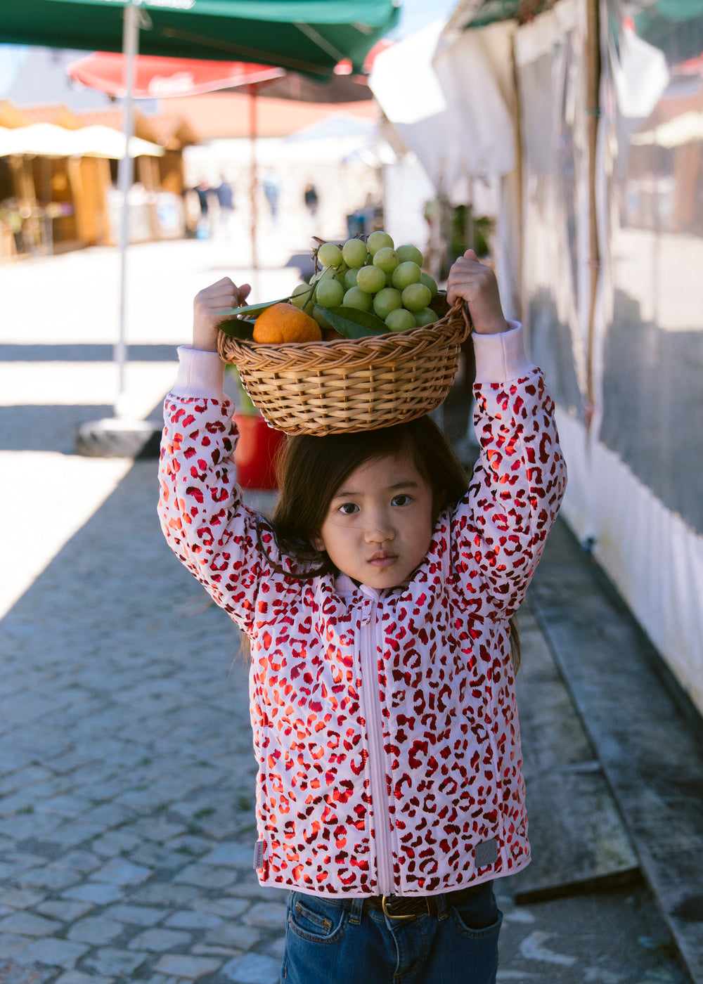 Child wearing a fluorescent red thermal jacket carrying a fruit basket with leopard print.