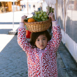 Child wearing a fluorescent red thermal jacket carrying a fruit basket with leopard print.