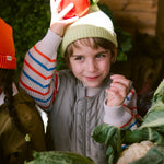 Child wearing a striped sweater in an outdoor environment among vegetables.