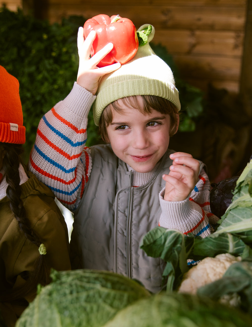 Children with a light green striped hat among vegetables for children