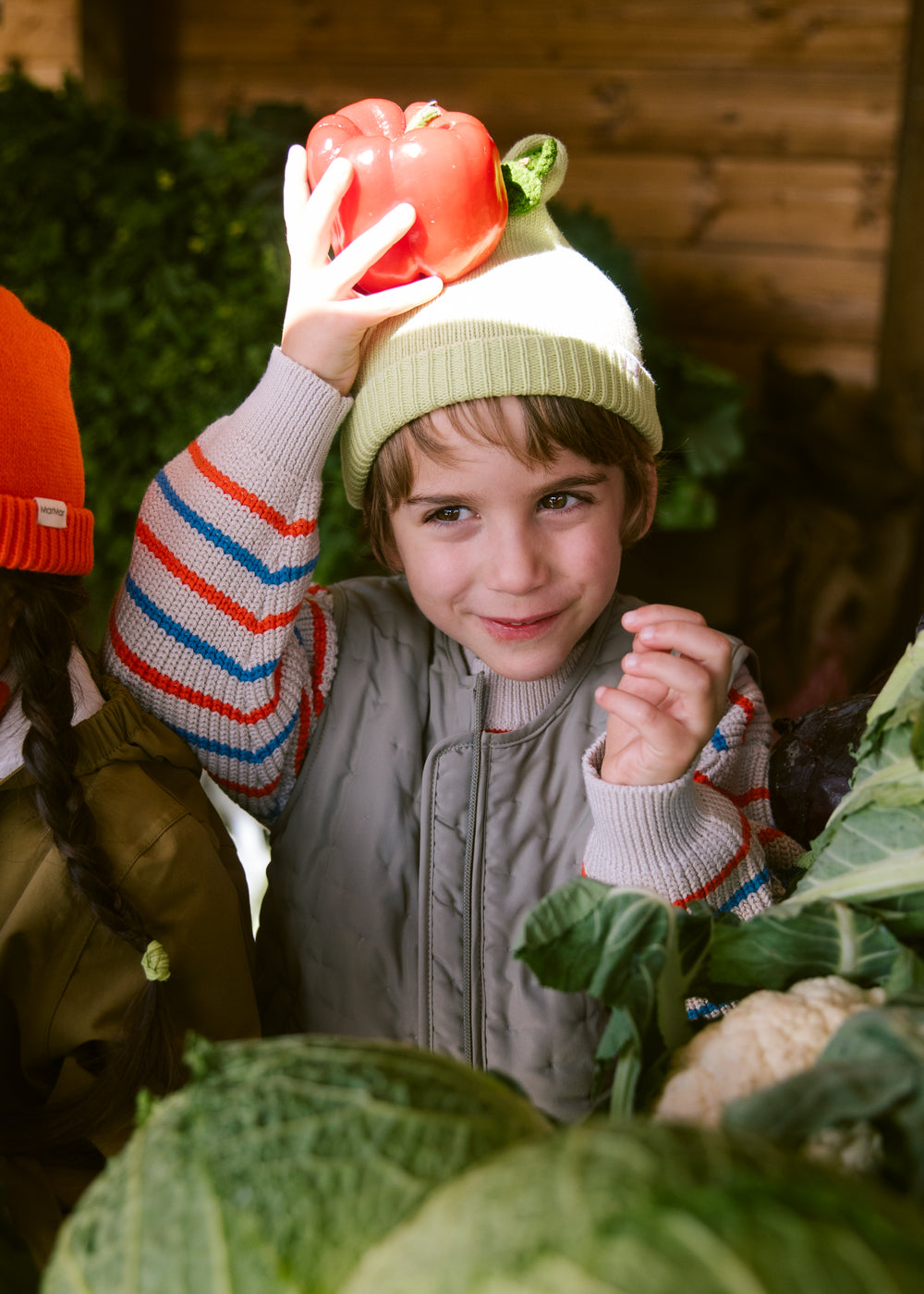 Children with a light green striped hat among vegetables for children