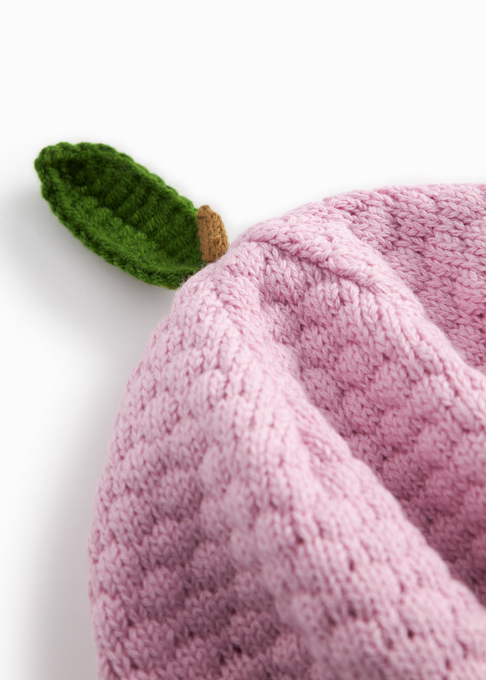 Red knitted baby hat with a green leaf.