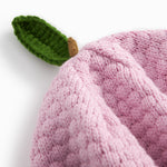 Red knitted baby hat with a green leaf.