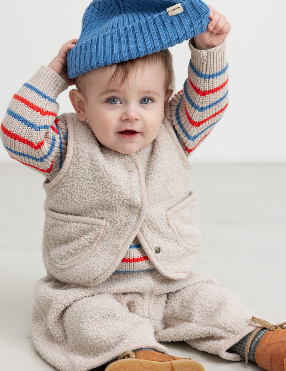 Baby wearing a knitted hat, striped shirt, and vest.