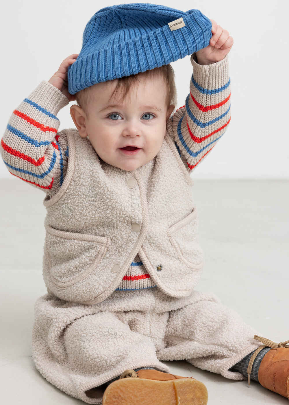 Baby wearing a knitted hat, striped shirt, and vest.