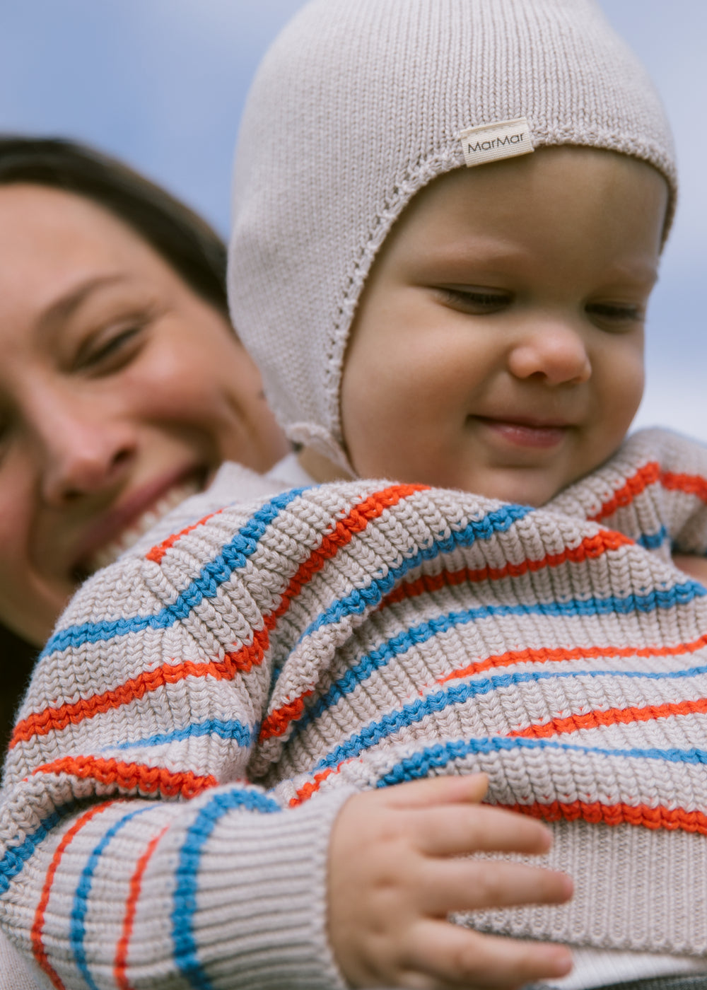 Baby is wearing a striped sweater and hat outdoors.