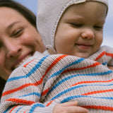 Baby is wearing a striped sweater and hat outdoors.