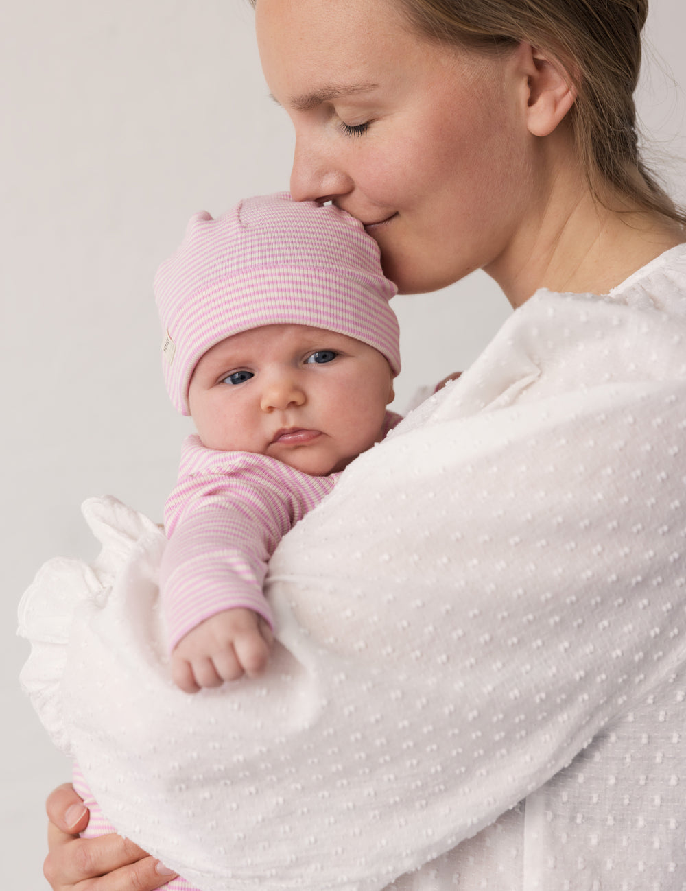 Baby wearing a yellow hat held in the arms of an adult.