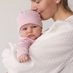 Baby wearing a yellow hat held in the arms of an adult.
