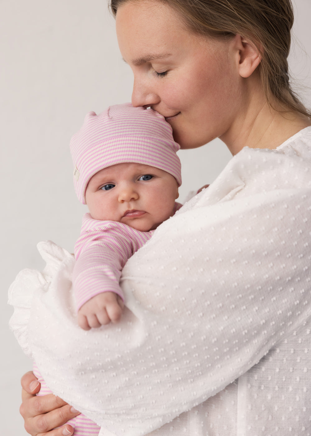 Baby wearing a yellow hat held in the arms of an adult.