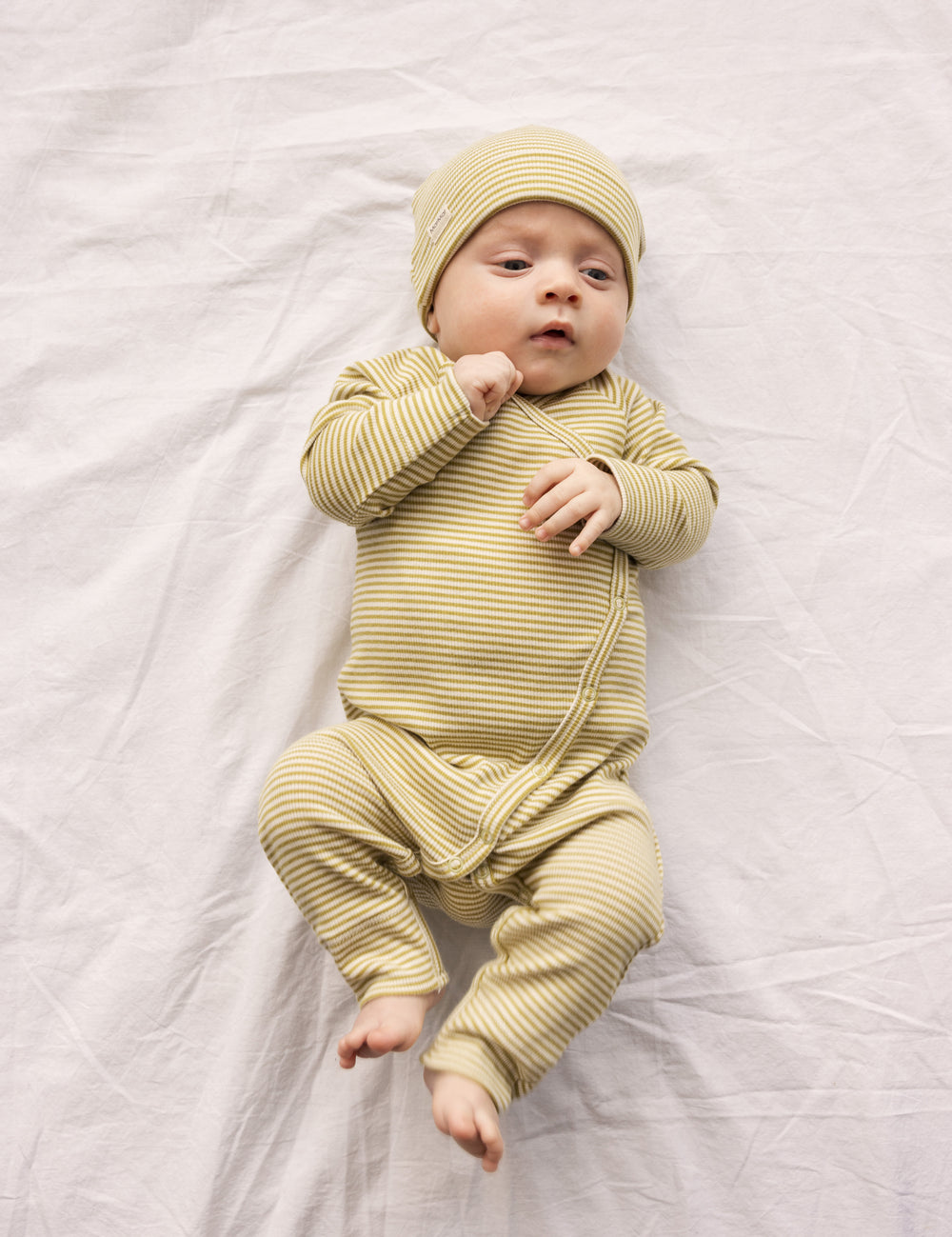 Baby wearing a green-striped onesie and matching hat.