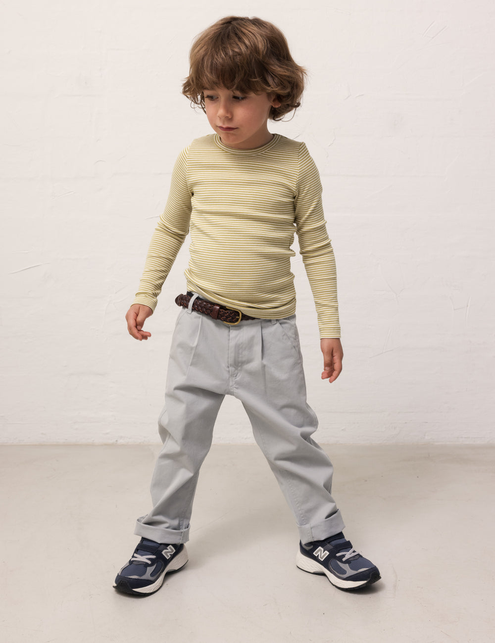Child wearing a green-striped long-sleeved shirt and light blue chino pants.