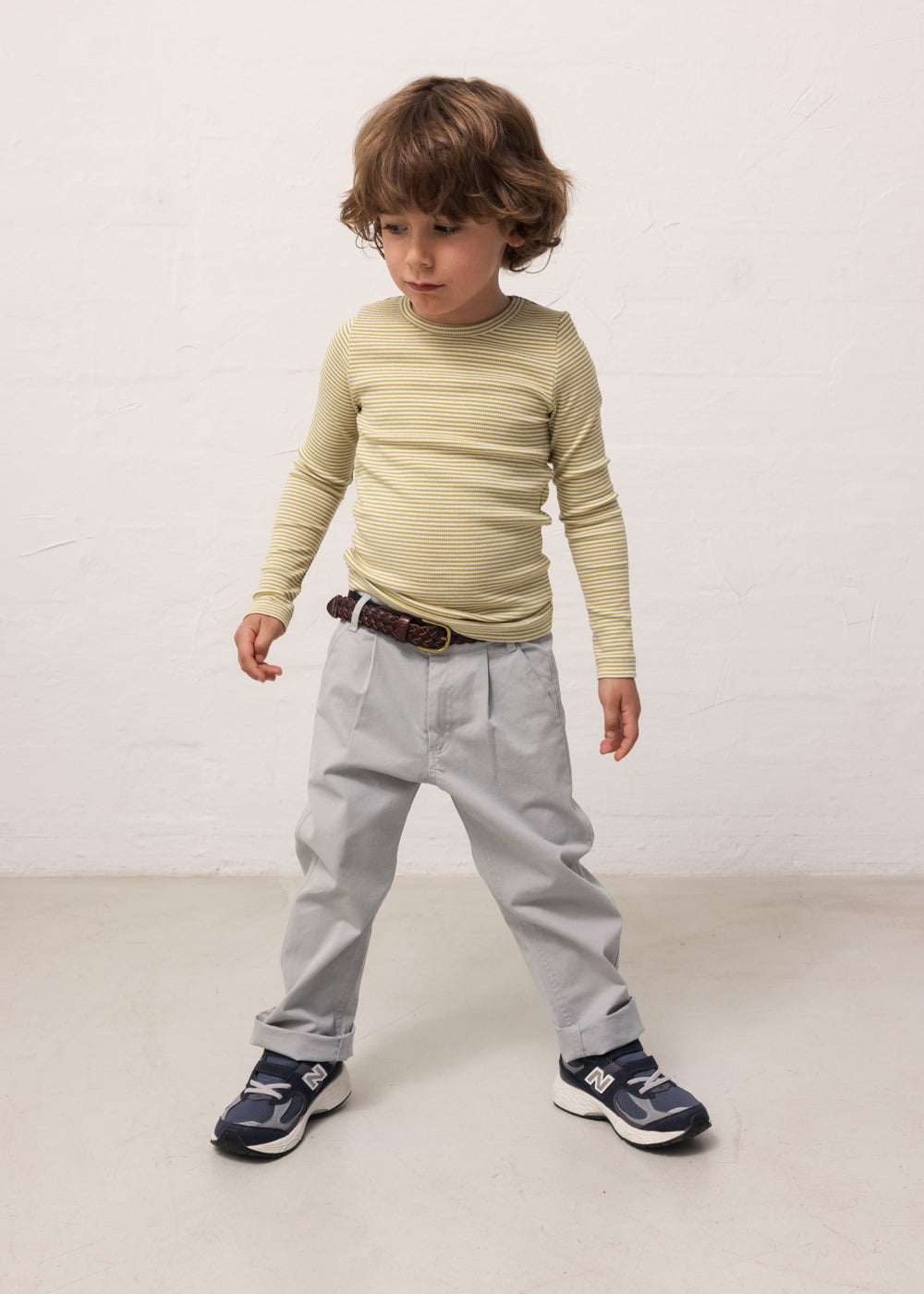 Child wearing a green-striped long-sleeved shirt and light blue chino pants.
