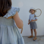 Child wearing a light dress and a hat with a mirror.