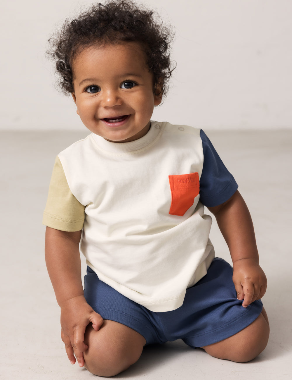 Baby wearing a raw white T-shirt with contrast sleeves and pocket.