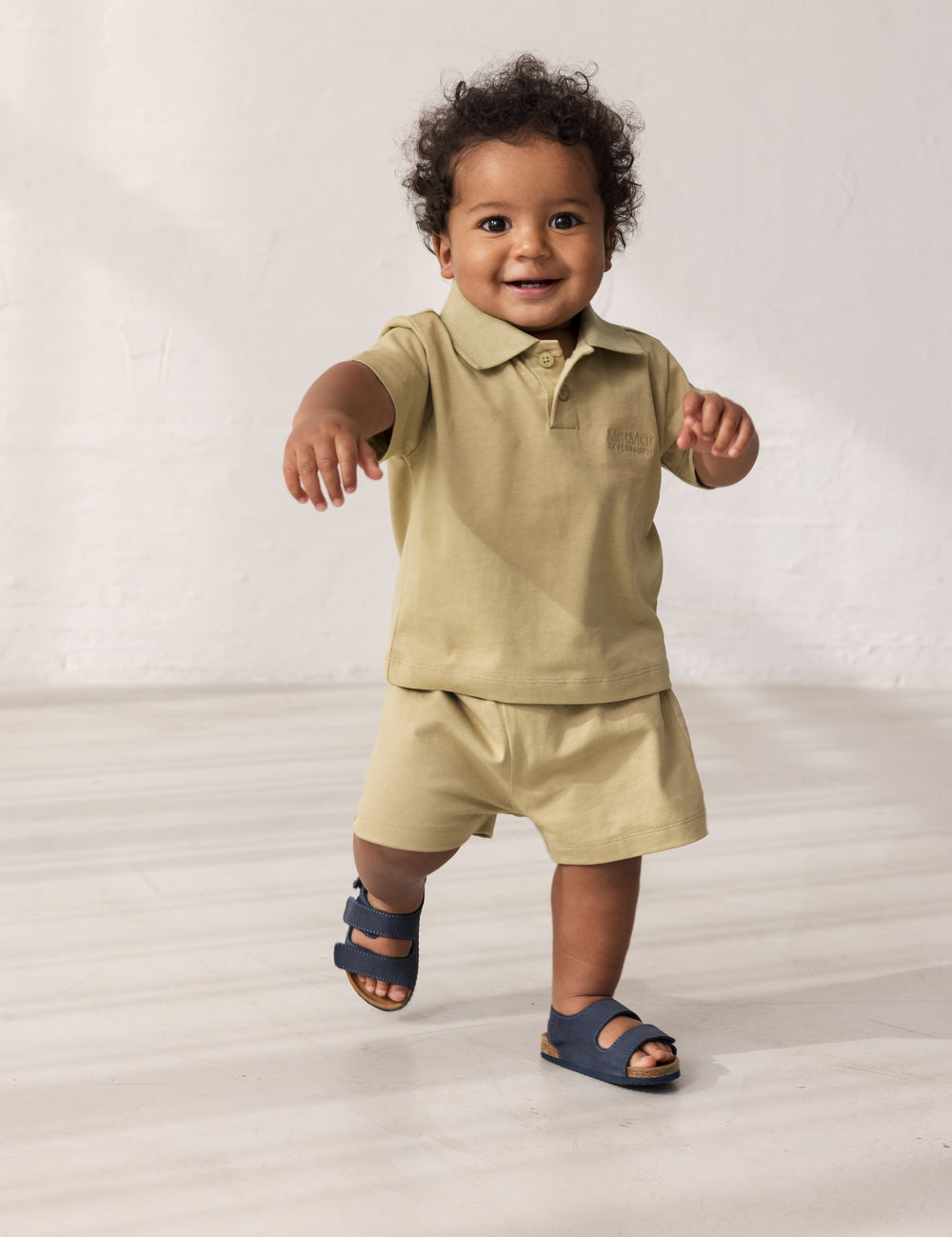 Baby wearing short-sleeved beige polo t-shirt with collar and buttons.