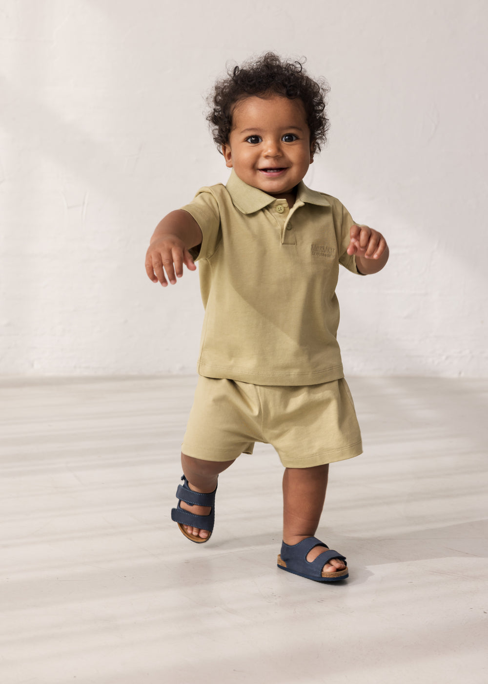 Baby wearing short-sleeved beige polo t-shirt with collar and buttons.