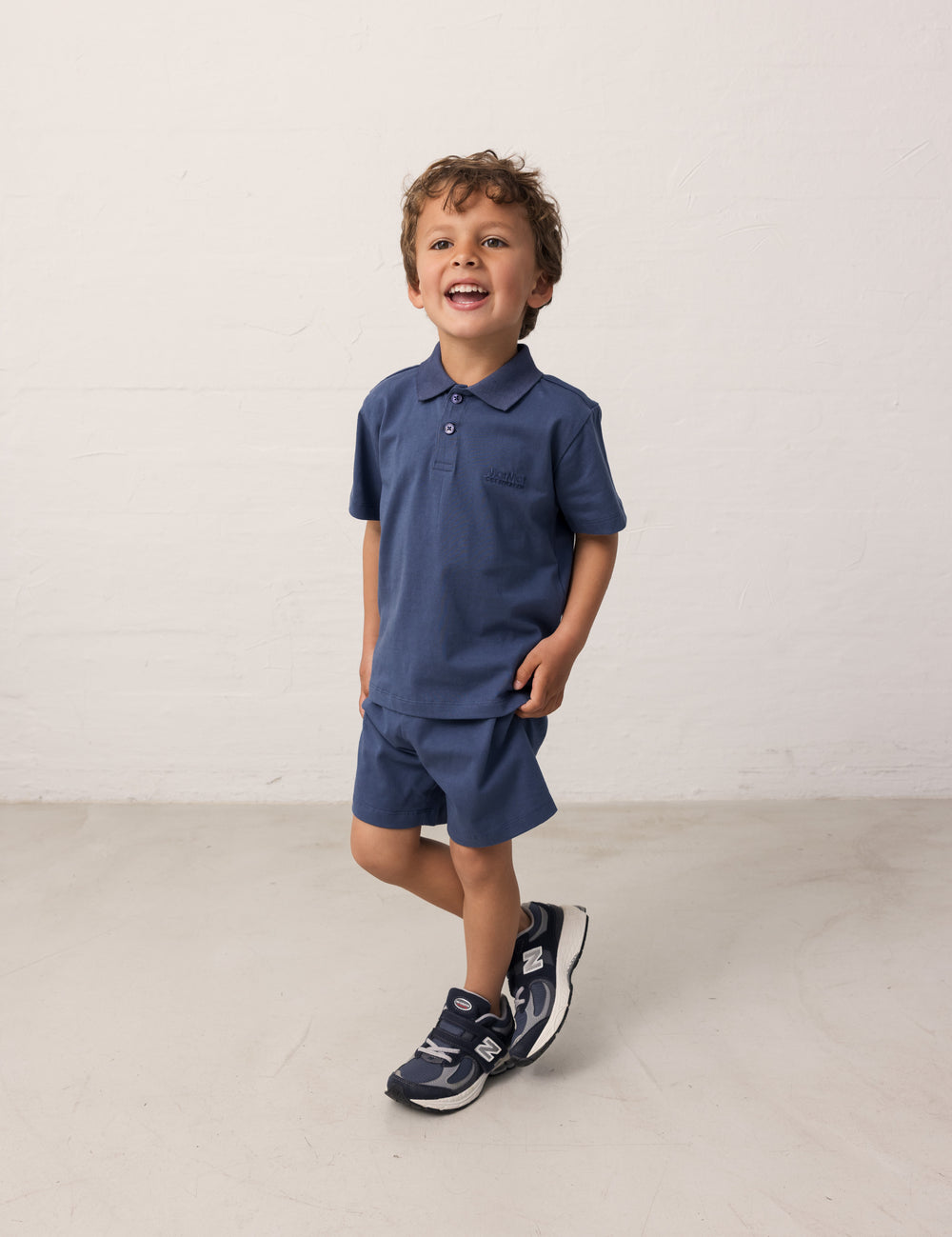 Boy wearing a short-sleeved blue polo t-shirt with a collar and buttons and matching shorts