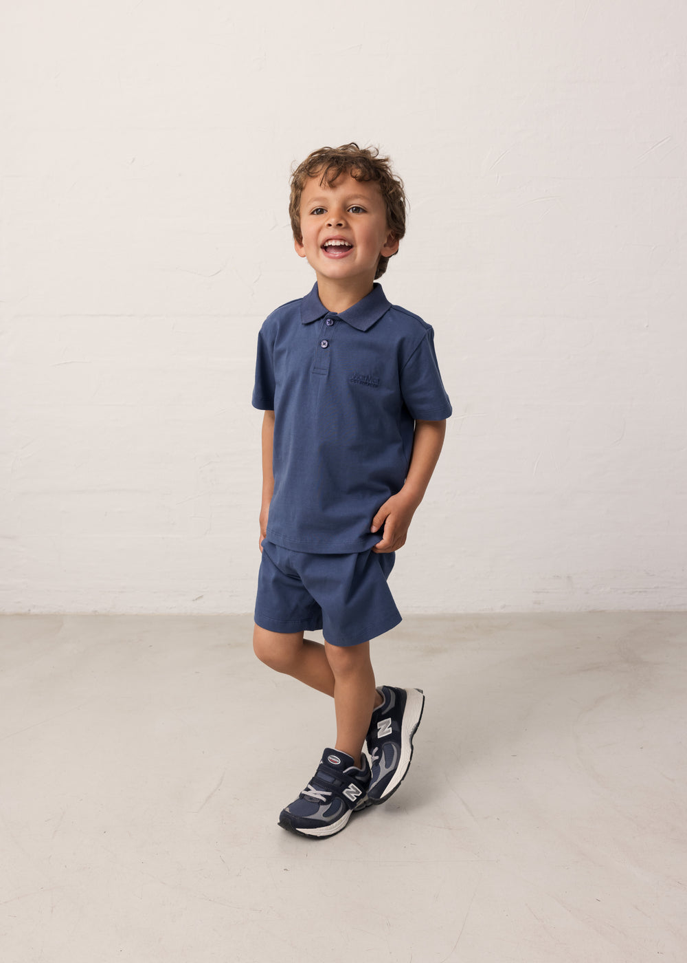 Boy wearing a short-sleeved blue polo t-shirt with a collar and buttons and matching shorts