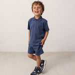Boy wearing a short-sleeved blue polo t-shirt with a collar and buttons and matching shorts