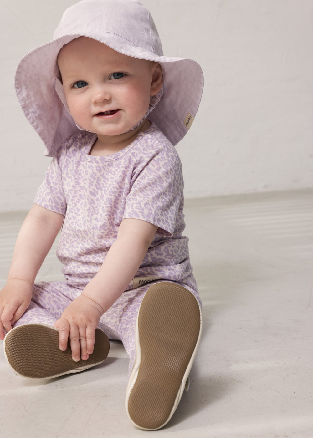 Baby wearing a light lavender summer hat and a lavender leopard-patterned outfit.