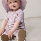 Baby wearing a light lavender summer hat and a lavender leopard-patterned outfit.