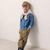 Child wearing a blue denim shirt and brown pants.