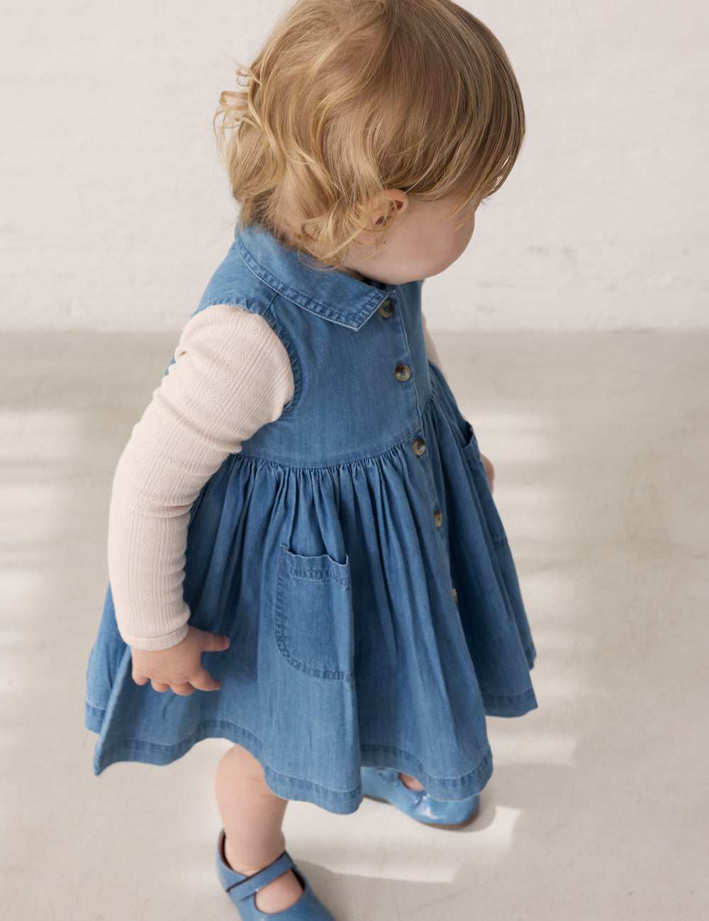 Child wearing a blue denim dress with buttons and a long-sleeved bright yellow body.
