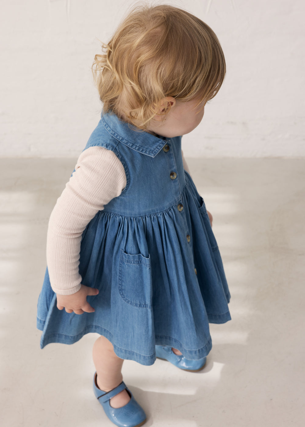 Child wearing a blue denim dress with buttons and a long-sleeved bright yellow body.