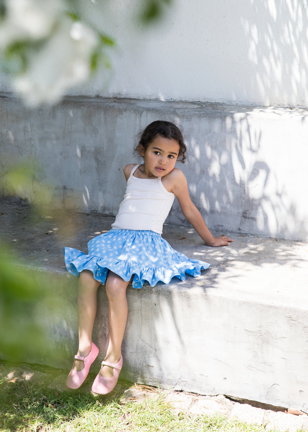 Wearing a white top and blue bottoms with small floral prints, as well as bright red shoes.
