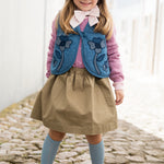 Child wearing a denim vest with a dress and a sunhat.