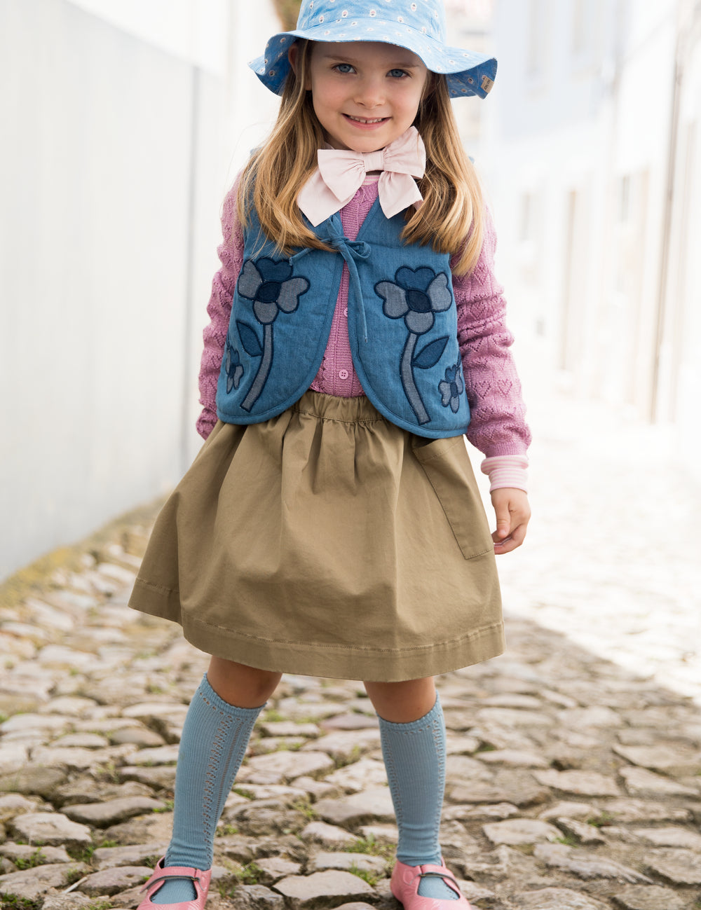Child wearing a blue sunhat, vest, and dress