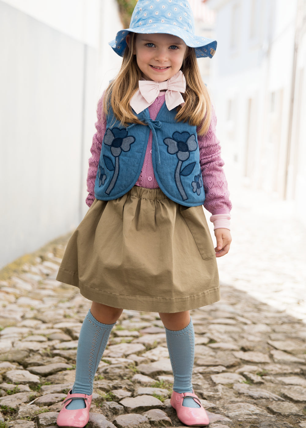 Child wearing a blue denim vest with floral embroidery, shorts, and a sunhat.