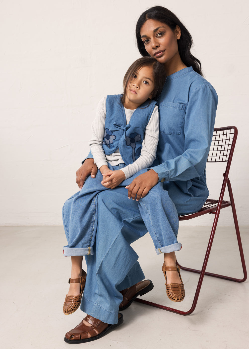Adult wearing blue denim pants and shirt sitting with a child.