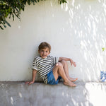 Child wearing a striped shirt and denim shorts.