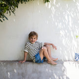 Child wearing a striped shirt and denim shorts.