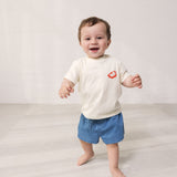 Baby wearing a white T-shirt with Mumin print and denim shorts.