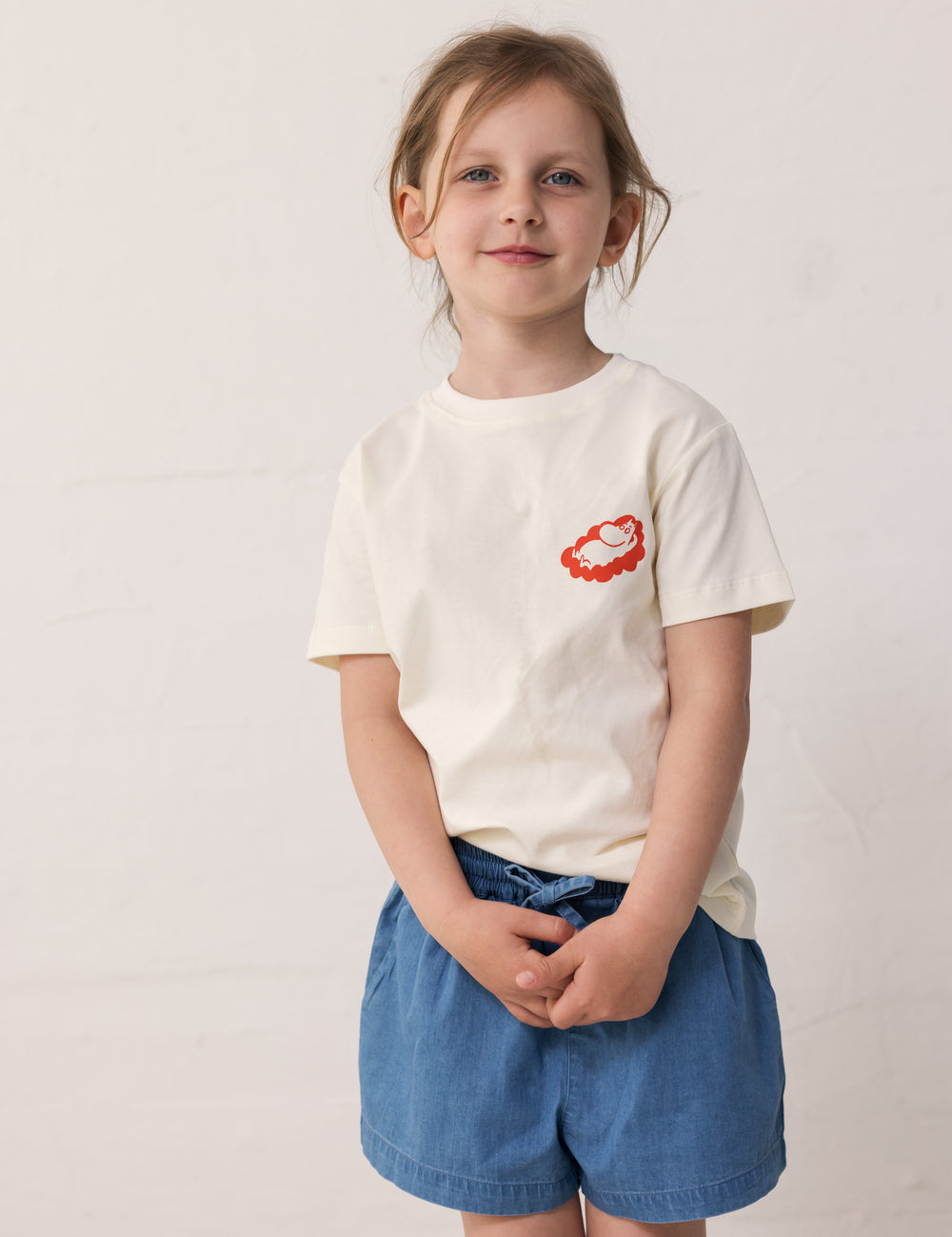 Children wearing a white T-shirt with Mumin print and denim shorts.