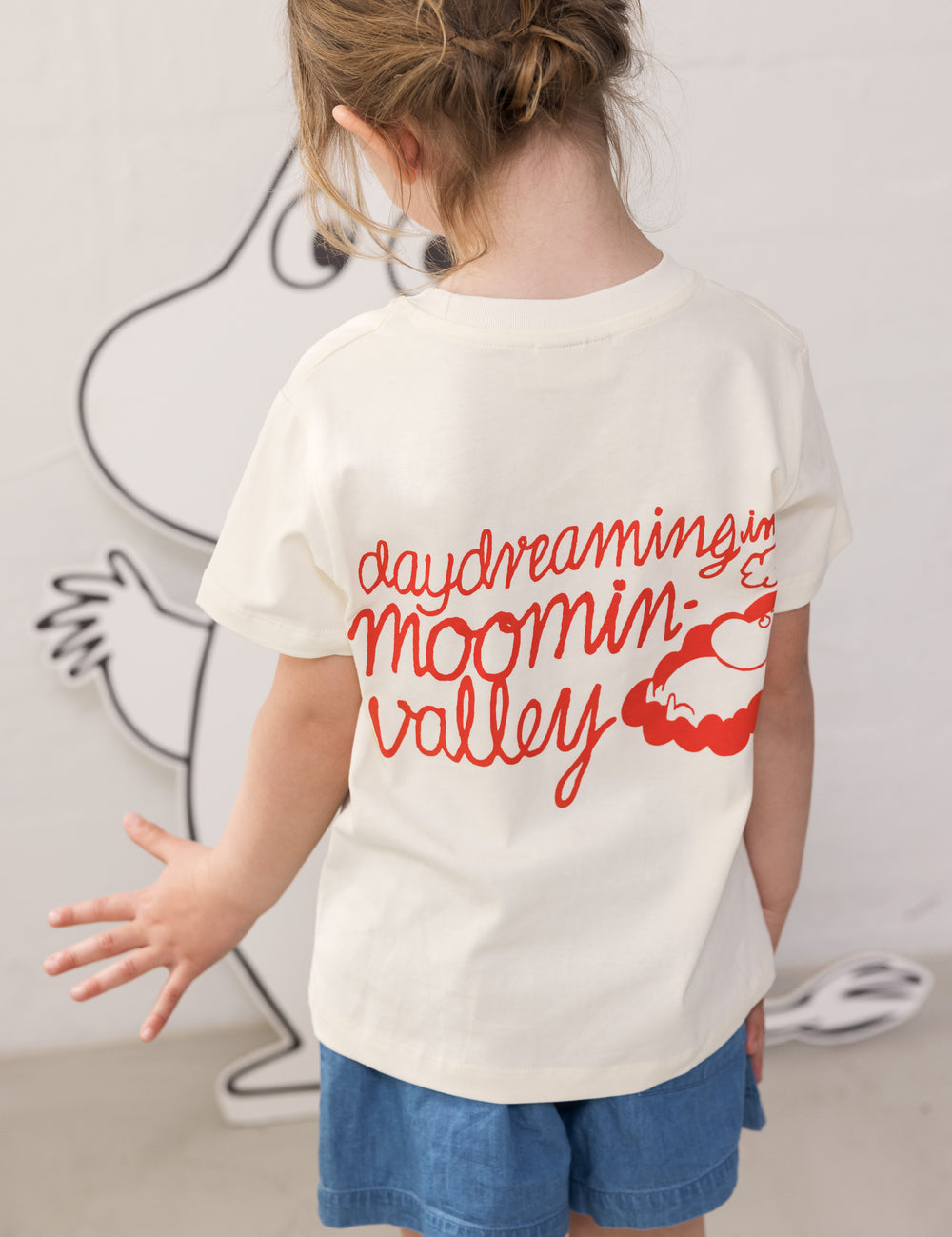 Children wearing a white T-shirt with Mumin print and denim shorts.