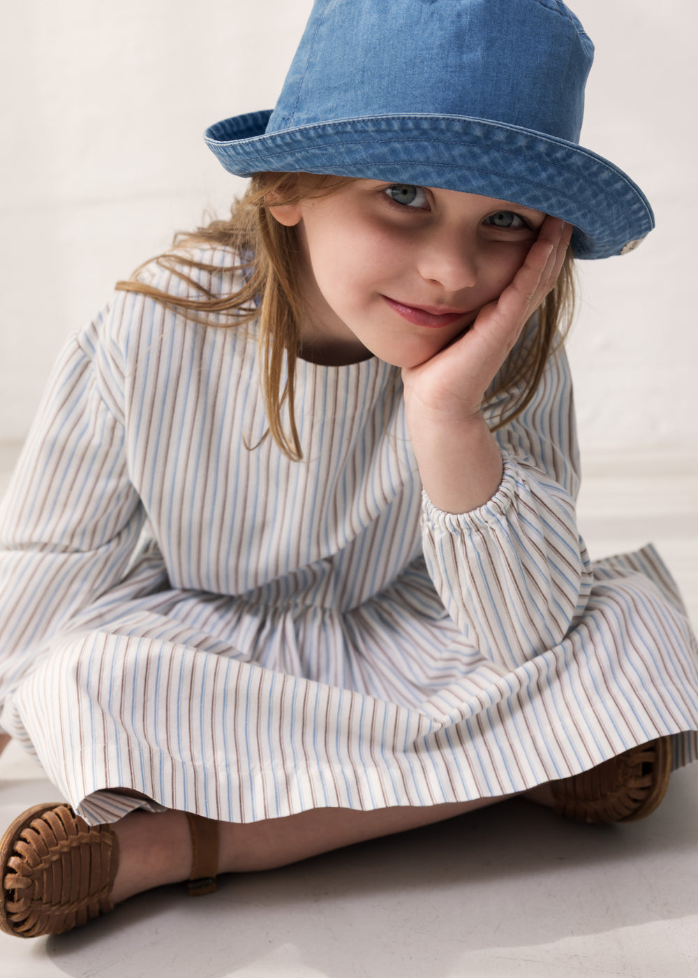 A child wearing a blue cap and a striped dress.