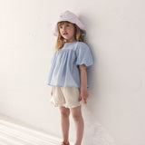 Pige iført kortærmet bluse til børn med puffærmer og fint broderimønster, lyse shorts og solhat

Girl wearing a short-sleeved blouse with puffed sleeves and a fine embroidery pattern, light shorts and a sun hat