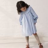 Wearing a light blue long-sleeved dress with an embroidery pattern.