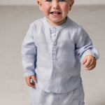 Baby wearing a long-sleeved light blue shirt with a crew neck and front buttoning, along with matching bloomers.